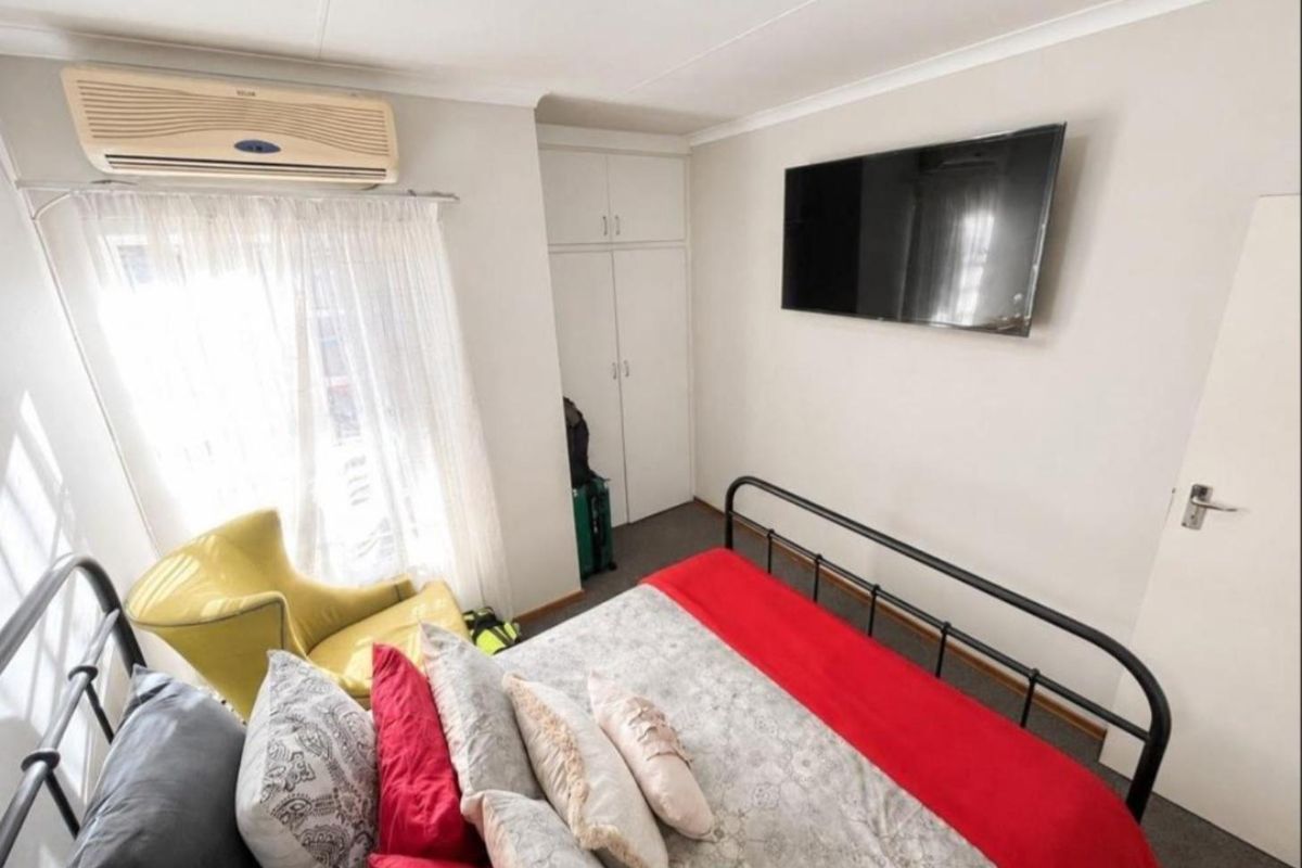 A functional bedroom featuring built-in cupboards, carpeted flooring, and a wall-mounted air conditioning unit for climate control.