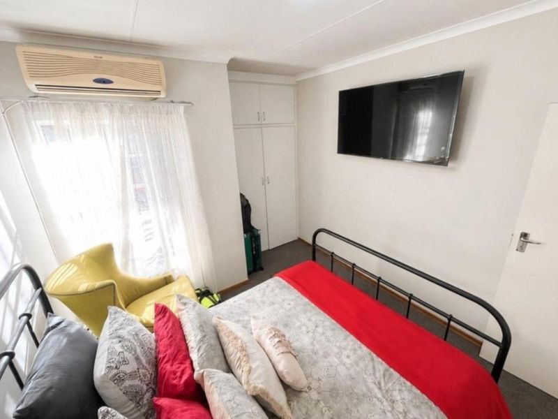 A functional bedroom featuring built-in cupboards, carpeted flooring, and a wall-mounted air conditioning unit for climate control.