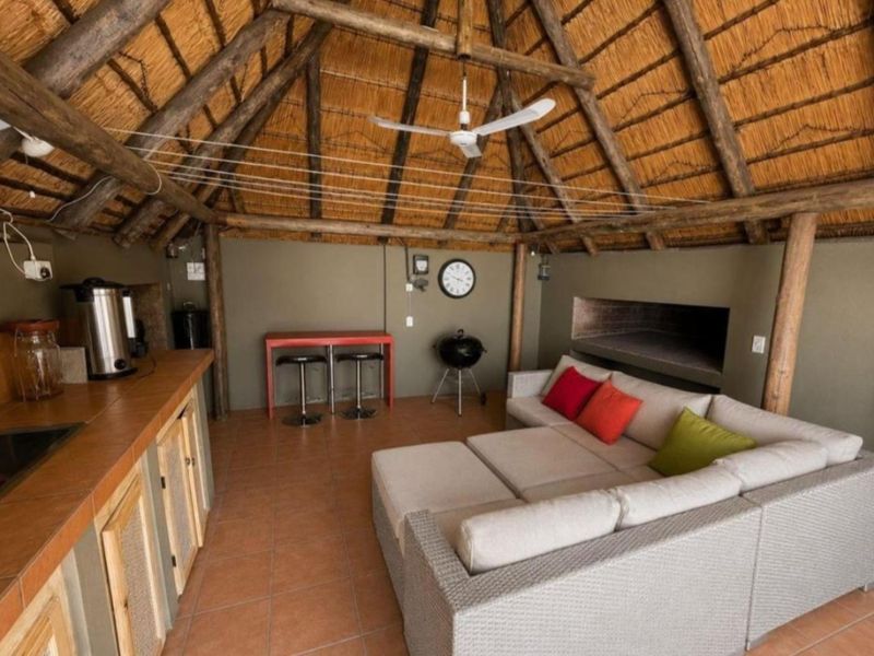 Covered outdoor entertainment area featuring a traditional thatched roof, exposed timber beams, built-in braai, and tiled flooring, ideal for relaxed social gatherings.
