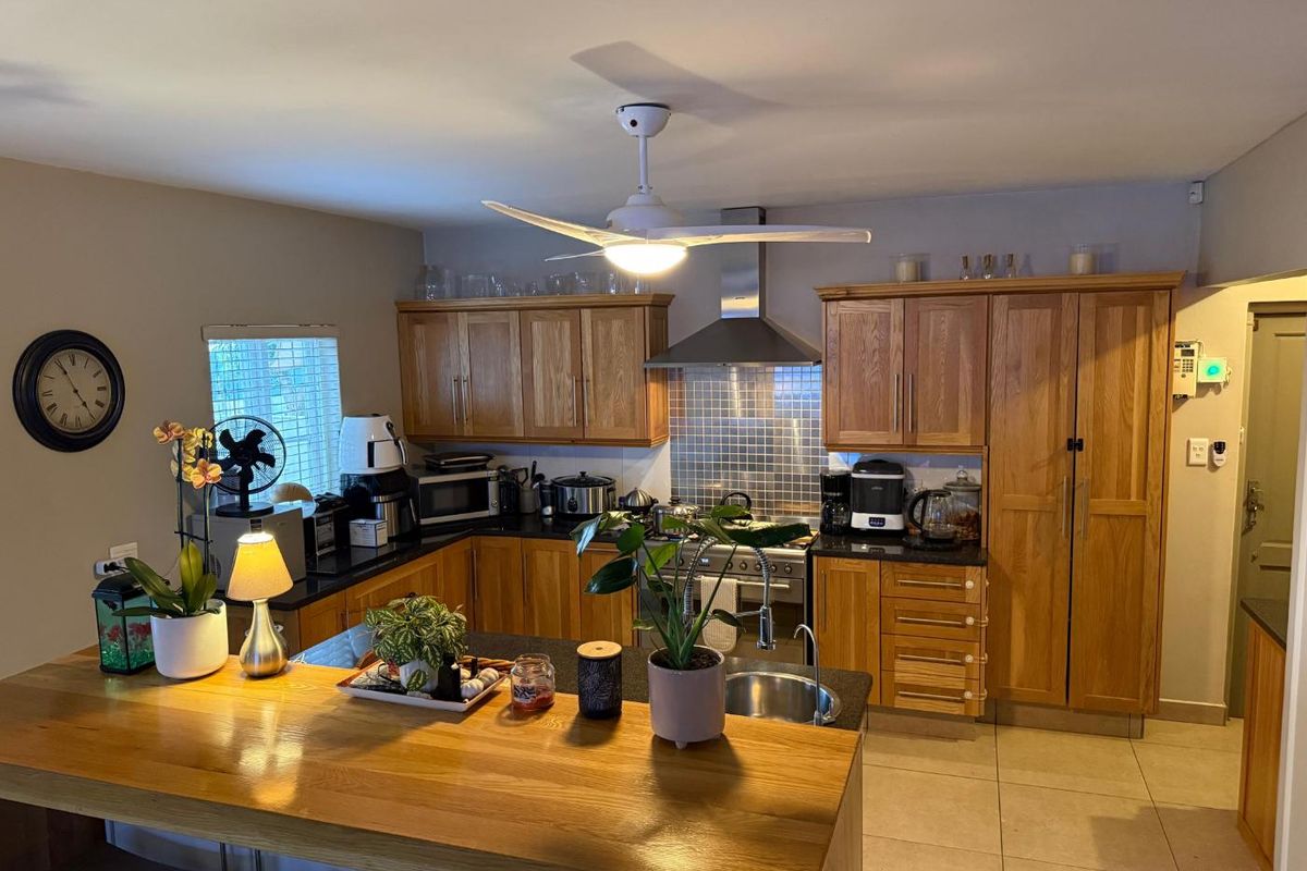 A functional kitchen featuring wooden cabinetry, granite countertops, a tiled backsplash, and a breakfast bar, complemented by a central ceiling fan.