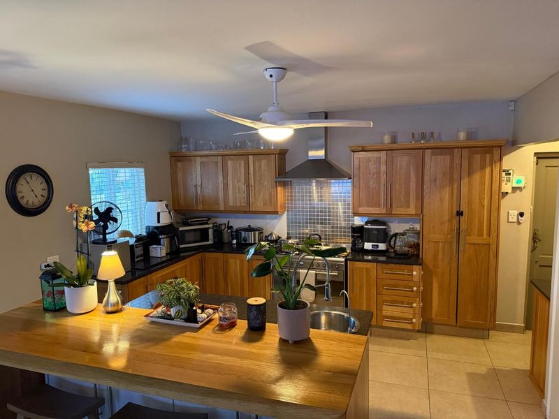 A functional kitchen featuring wooden cabinetry, granite countertops, a tiled backsplash, and a breakfast bar, complemented by a central ceiling fan.