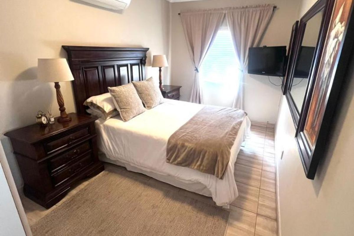 A well-maintained bedroom featuring tiled flooring, a wall-mounted split-system air conditioner, and neutral wall finishes.