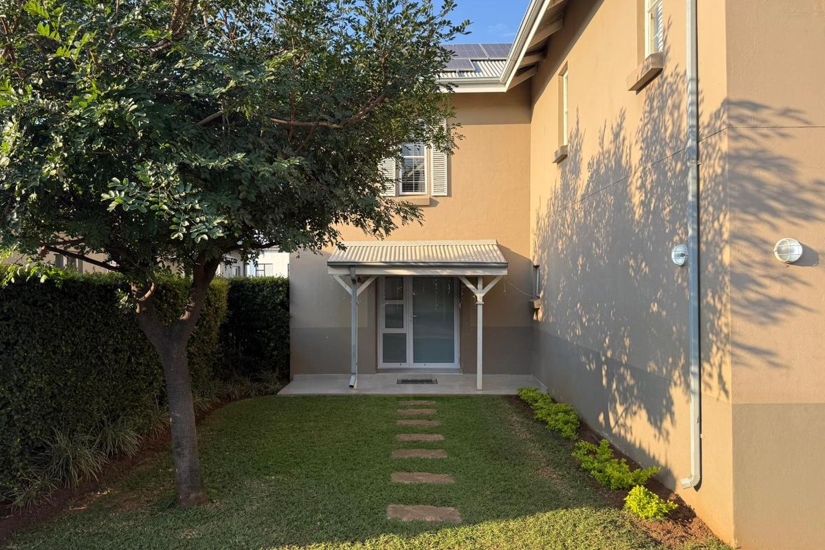 Rear exterior view of the house featuring a small covered patio, landscaped garden with a stone path, and visible solar panels on the roof.