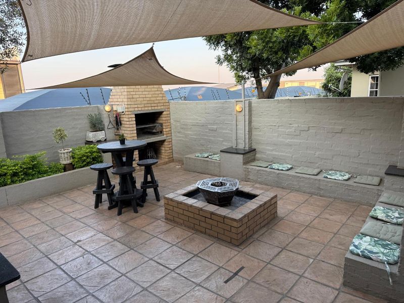 Outdoor patio area featuring a built-in brick braai, integrated brick seating, a central fire pit, and overhead shade sails.