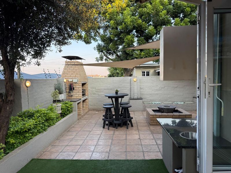 Outdoor patio area featuring a built-in brick braai, granite prep counter with sink, built-in bench seating, and shade sail coverage.