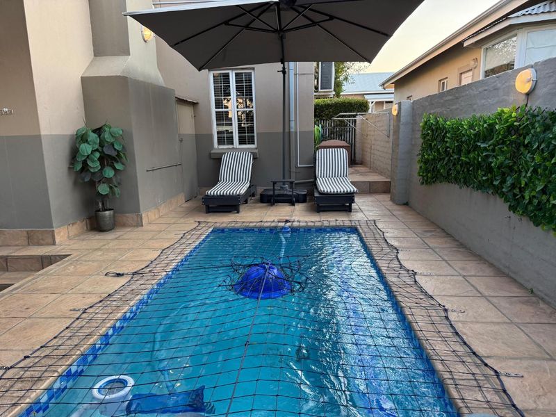 A compact outdoor pool area featuring a tiled surround, boundary wall, and integrated exterior lighting, providing a functional space for relaxation.