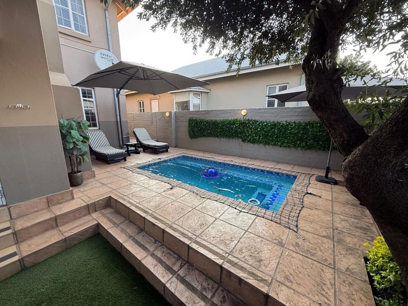 Compact outdoor pool area featuring a tiled deck, boundary wall with integrated lighting, and artificial grass section, perfect for low-maintenance outdoor relaxation.