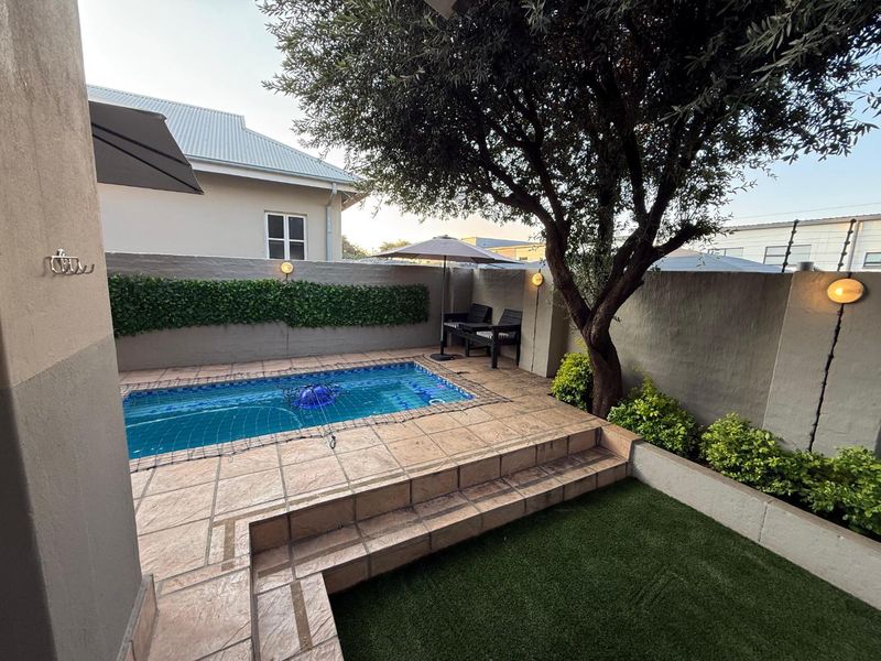 Compact outdoor pool area featuring a tiled surround, artificial lawn, and perimeter boundary walls with integrated lighting.