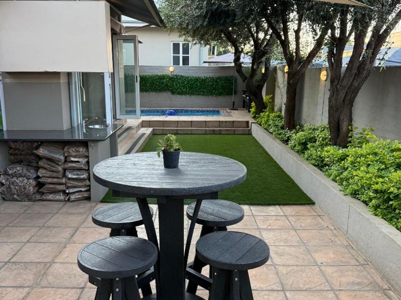Covered patio area featuring a built-in braai, shade sail, and tiled flooring, overlooking a landscaped garden and swimming pool.