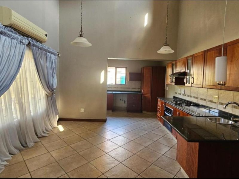 Spacious open-plan kitchen and living area featuring wooden cabinetry, granite countertops, gas hob, and tiled flooring, offering a functional layout for modern living.