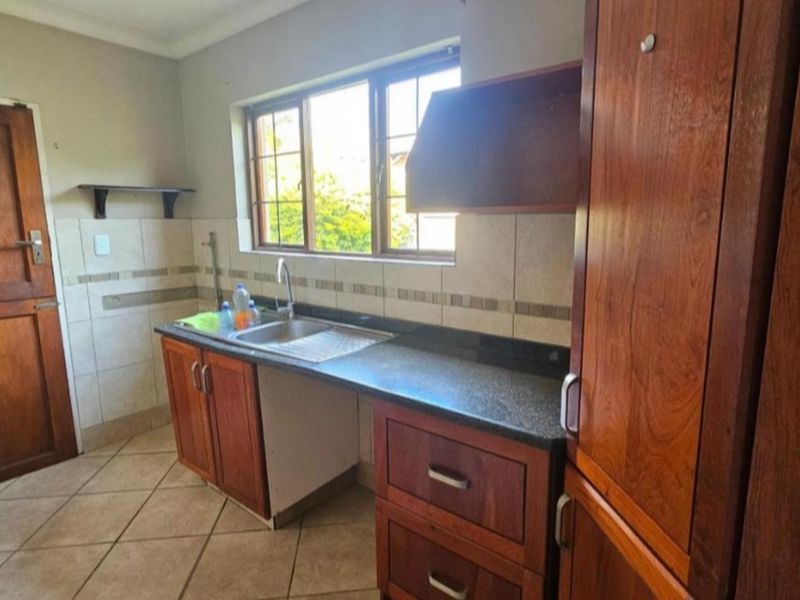 A functional kitchen featuring wooden cabinetry, stone countertops, a stainless steel sink, and tiled flooring with a neutral backsplash.