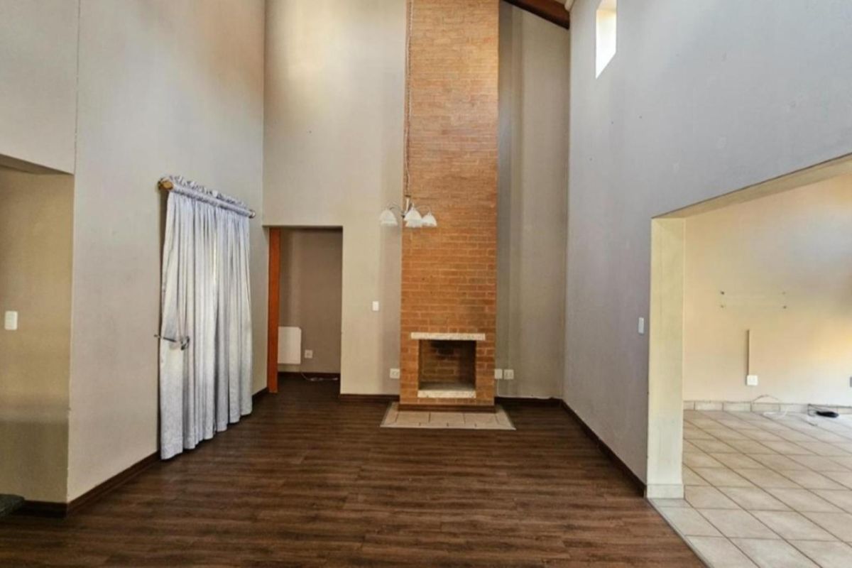 Spacious double-volume living area featuring a prominent brick fireplace, laminate flooring, and neutral wall tones, offering a versatile blank canvas for interior design.