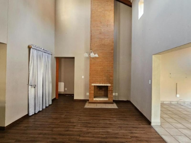 Spacious double-volume living area featuring a prominent brick fireplace, laminate flooring, and neutral wall tones, offering a versatile blank canvas for interior design.