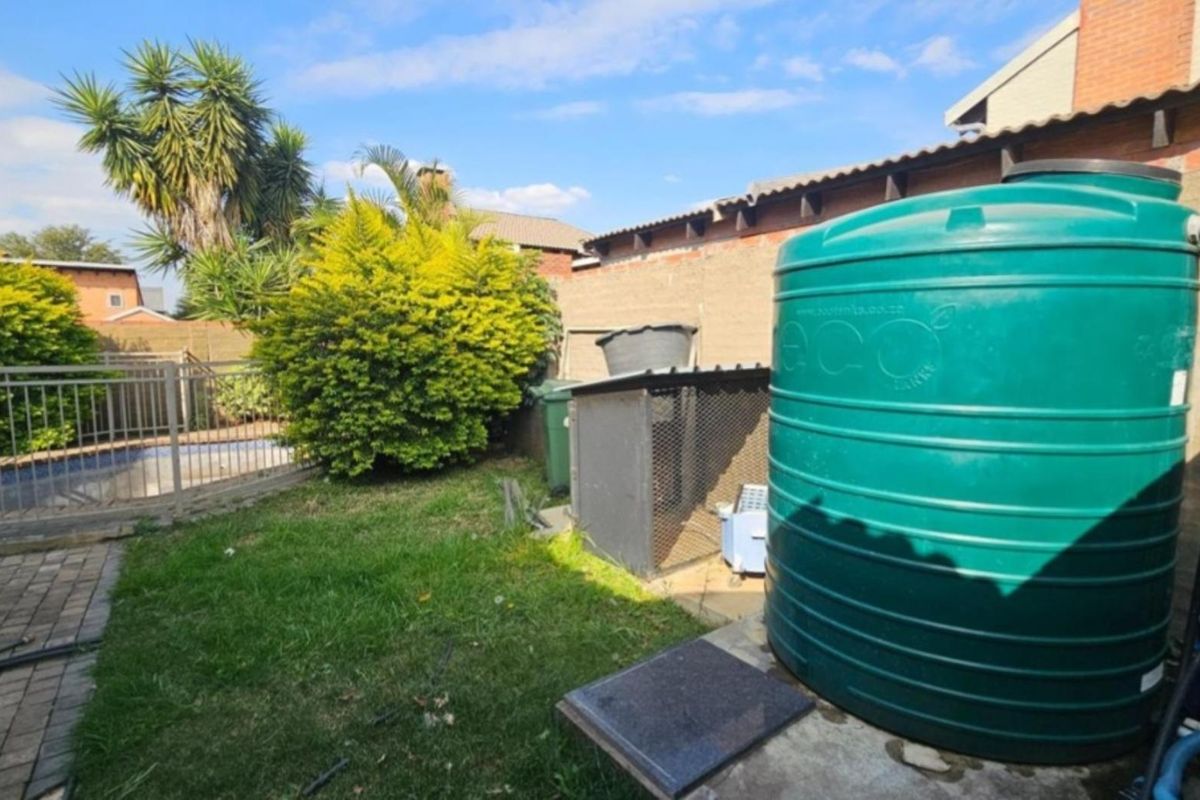Rear garden area featuring a large water storage tank, paved pathway, and perimeter walling with access to the swimming pool area.