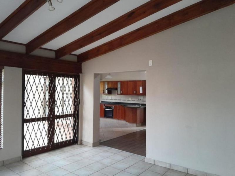 Open plan living area featuring exposed timber ceiling beams and tiled flooring, with a direct view into the adjacent kitchen space.