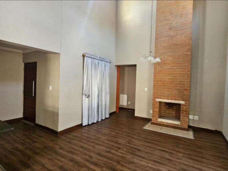 Spacious open-plan living area featuring a double-volume ceiling, brick fireplace, and durable laminate flooring, offering a versatile layout for modern living.