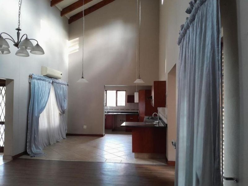 Spacious open-plan living and kitchen area featuring vaulted ceilings with exposed timber beams, tiled and laminate flooring, and a functional kitchen layout.