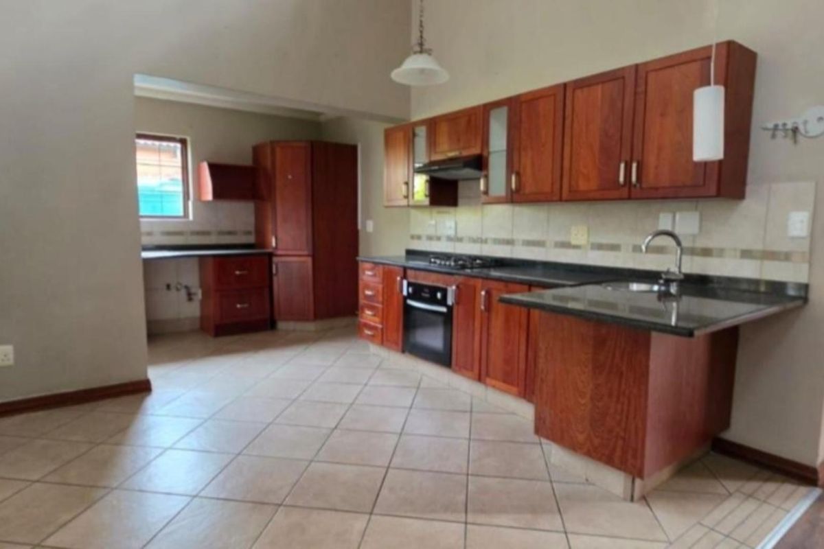 A functional kitchen featuring wooden cabinetry, granite countertops, built-in oven, gas hob, and tiled flooring, offering a practical layout for daily cooking.