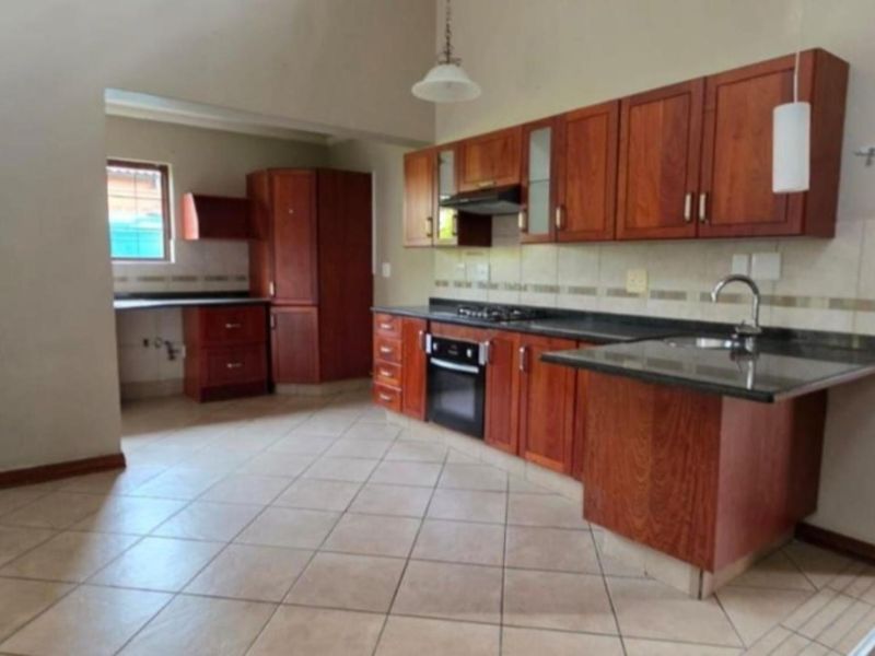 A functional kitchen featuring wooden cabinetry, granite countertops, built-in oven, gas hob, and tiled flooring, offering a practical layout for daily cooking.