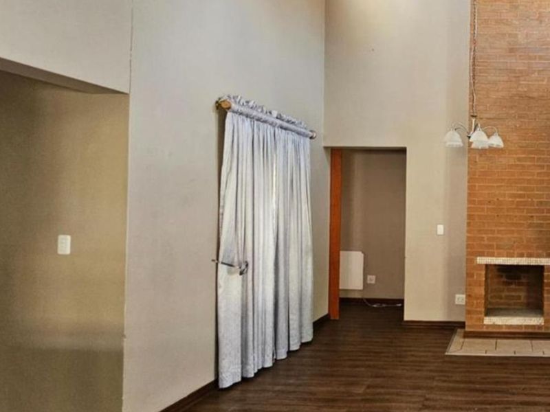 Spacious living area featuring high ceilings, dark laminate flooring, and a prominent floor-to-ceiling brick fireplace.