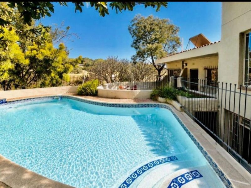 A well-maintained swimming pool area featuring decorative tile borders, metal safety fencing, and a solar water heating system on the adjacent building roof.