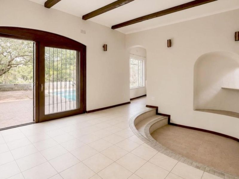 Spacious living area featuring exposed timber beams, a unique sunken floor section, an arched wall niche, and large sliding doors opening to the pool area.