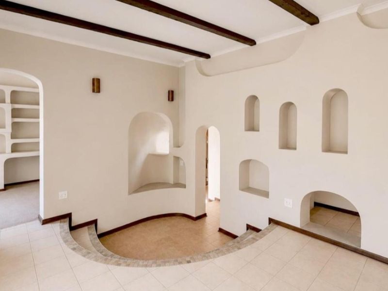 Spacious living area featuring a unique sunken floor design, decorative arched wall niches, exposed ceiling beams, and neutral tiled flooring throughout.