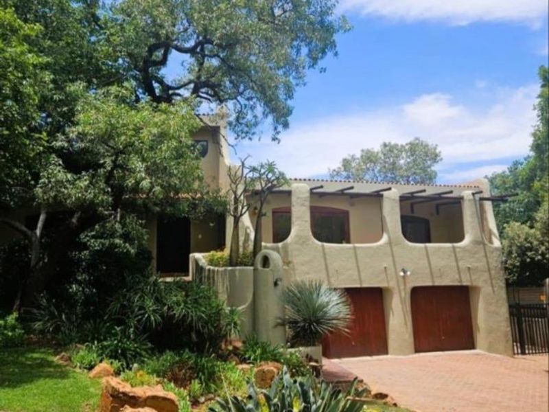 A charming double-story home featuring a stucco facade, double garage, paved driveway, and a spacious covered balcony surrounded by a lush, landscaped garden.