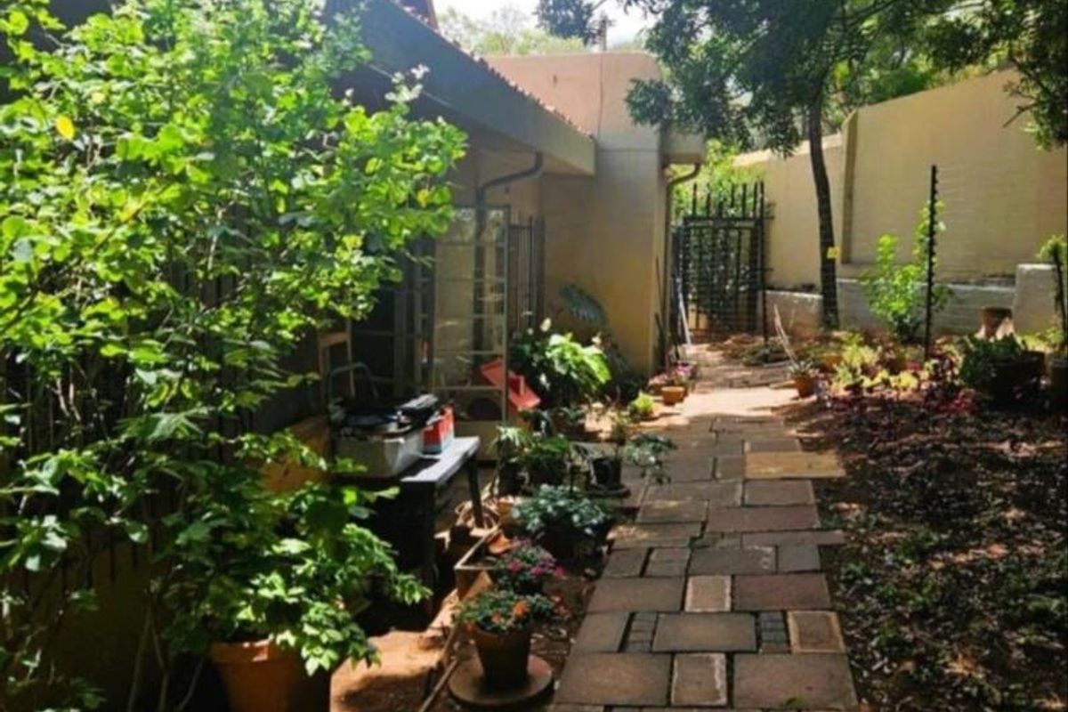 A rear garden pathway featuring stone paving, established greenery, and a secure boundary wall leading to a gated access point.