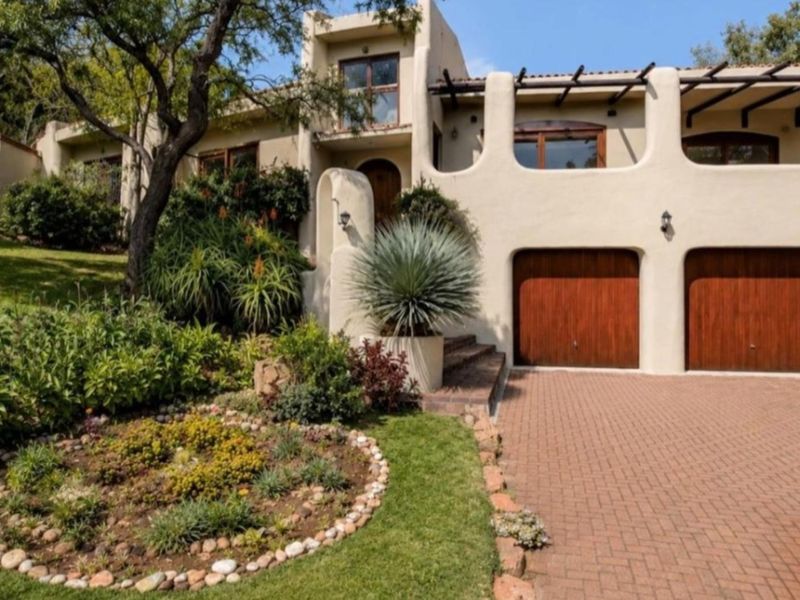 Attractive front elevation featuring a double garage, paved driveway, and well-maintained landscaped garden with unique architectural stucco detailing.