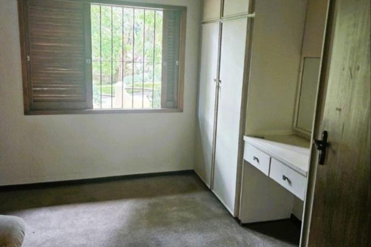 A bedroom featuring built-in cupboards, a vanity unit, exposed ceiling beams, and a window with security bars.