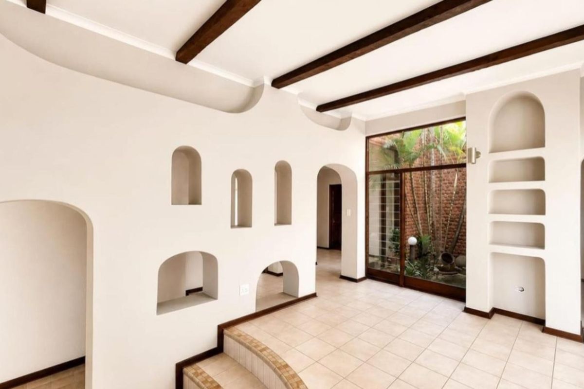 Spacious living area featuring unique architectural arched wall niches, exposed timber ceiling beams, tiled flooring, and a large glass door overlooking an internal courtyard.