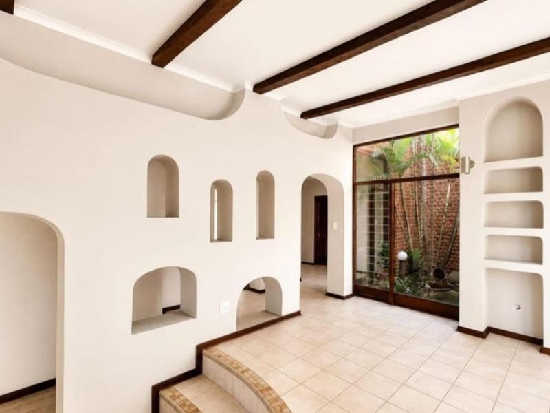 Spacious living area featuring unique architectural arched wall niches, exposed timber ceiling beams, tiled flooring, and a large glass door overlooking an internal courtyard.
