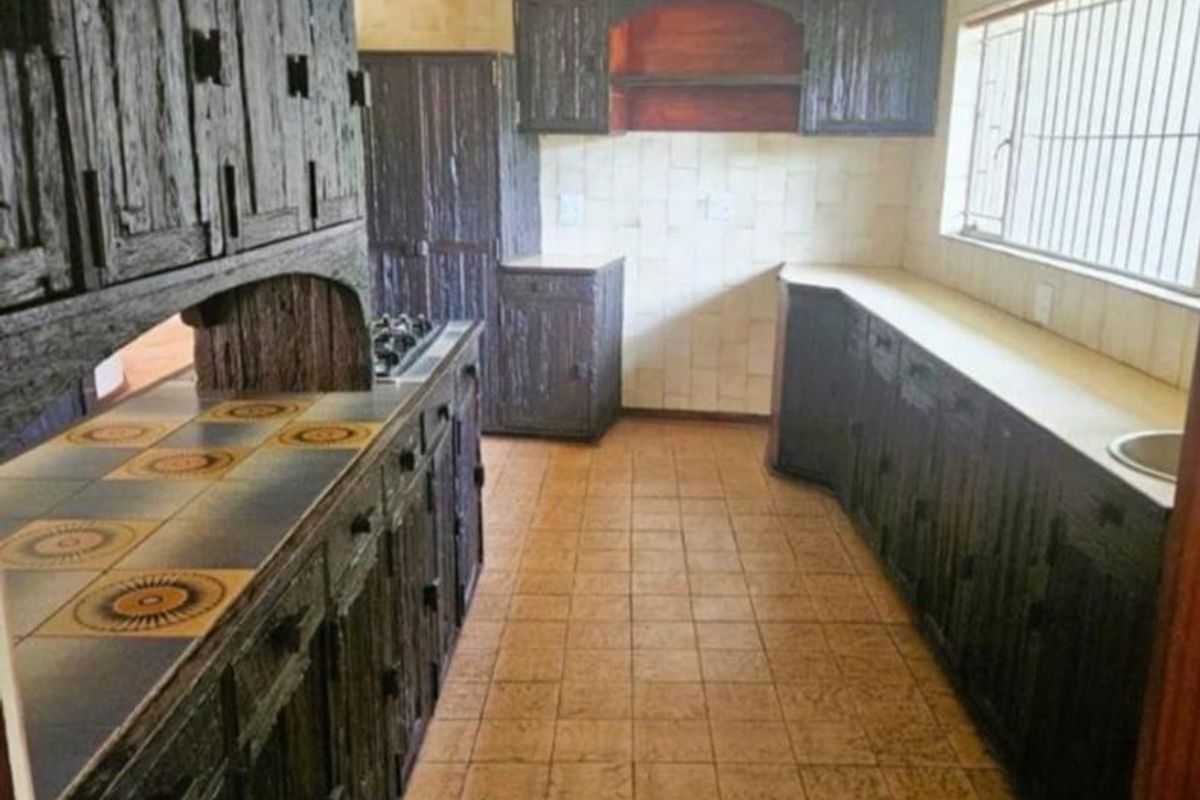 A dated kitchen featuring dark textured cabinetry, tiled countertops with integrated hob, and tiled flooring, offering significant potential for a modern renovation.