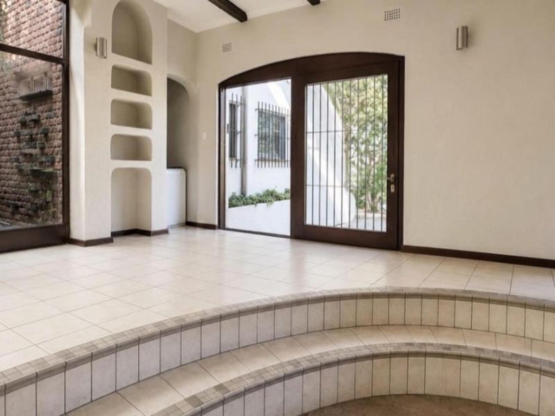 Spacious living area featuring tiled flooring, built-in arched shelving, exposed timber ceiling beams, and large arched glass doors leading to the exterior.