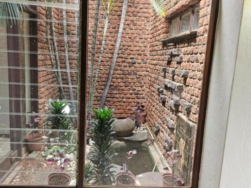 A private internal courtyard featuring exposed brick walls, a built-in water feature, and natural light through large louvre windows.