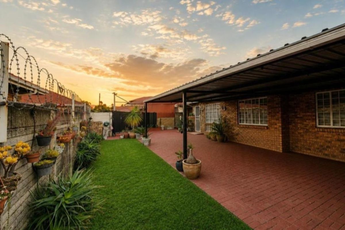 A well-maintained rear exterior area featuring a paved carport, a neat lawn, and a secure brick boundary wall with razor wire.