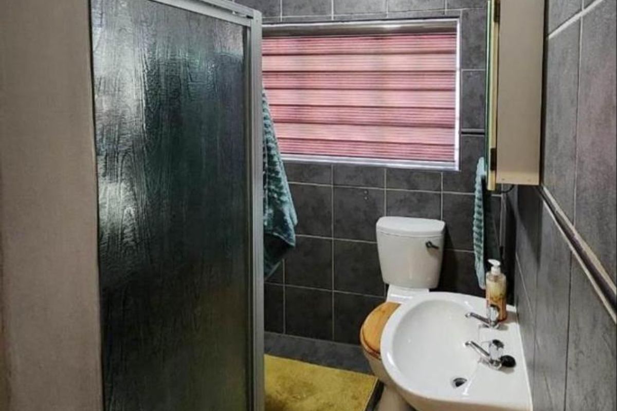 A functional bathroom featuring a shower enclosure, pedestal basin, and toilet, finished with dark grey wall and floor tiles.