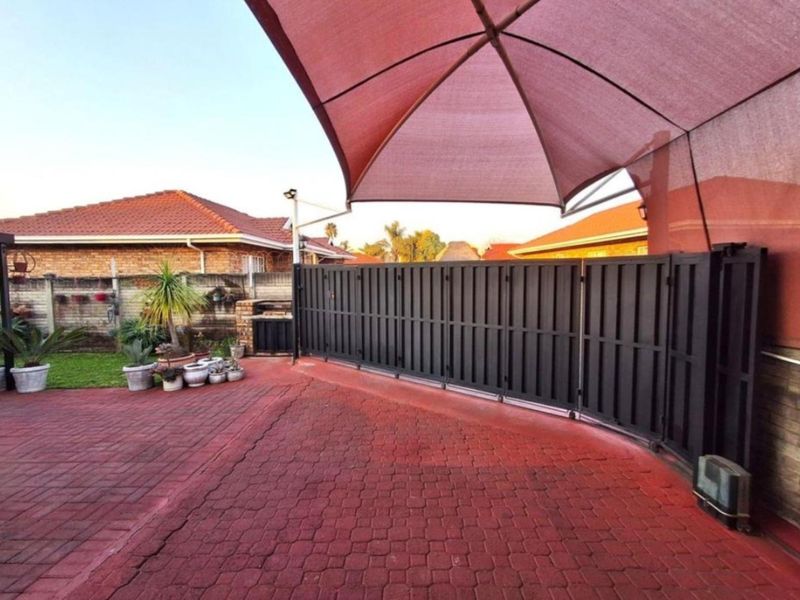 Front exterior area featuring a paved driveway, secure sliding gate, shade sail covering, and a built-in braai area.