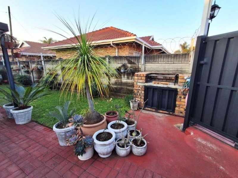 Rear garden area featuring a built-in brick braai, paved patio space, and perimeter walling with security fencing.