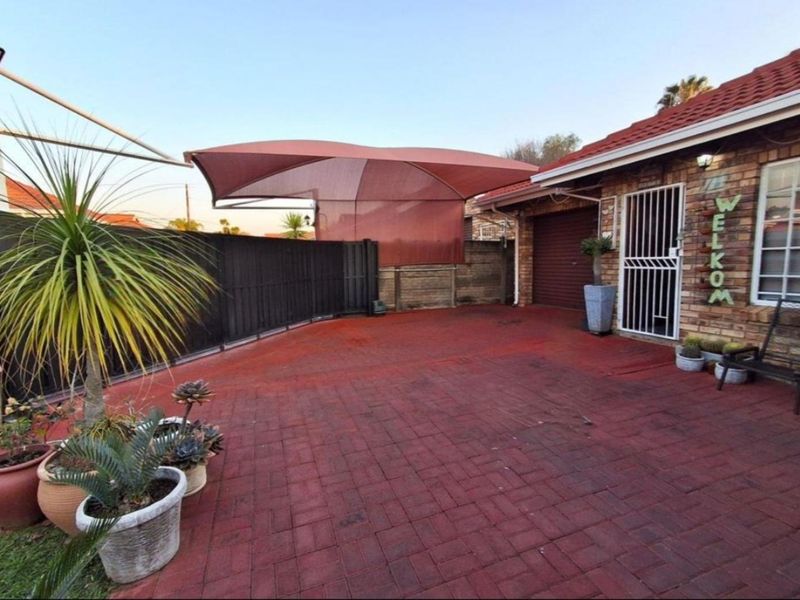 Front exterior area featuring brick paving, a shade sail for vehicle protection, and a secure entrance with a security gate and garage access.