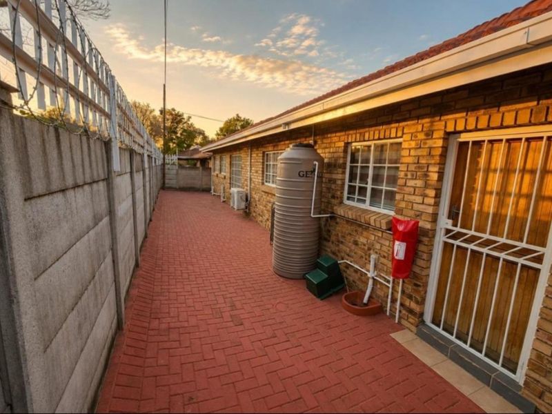A well-maintained rear exterior area featuring brick wall construction, paved pathways, a water storage tank, and secure perimeter fencing.