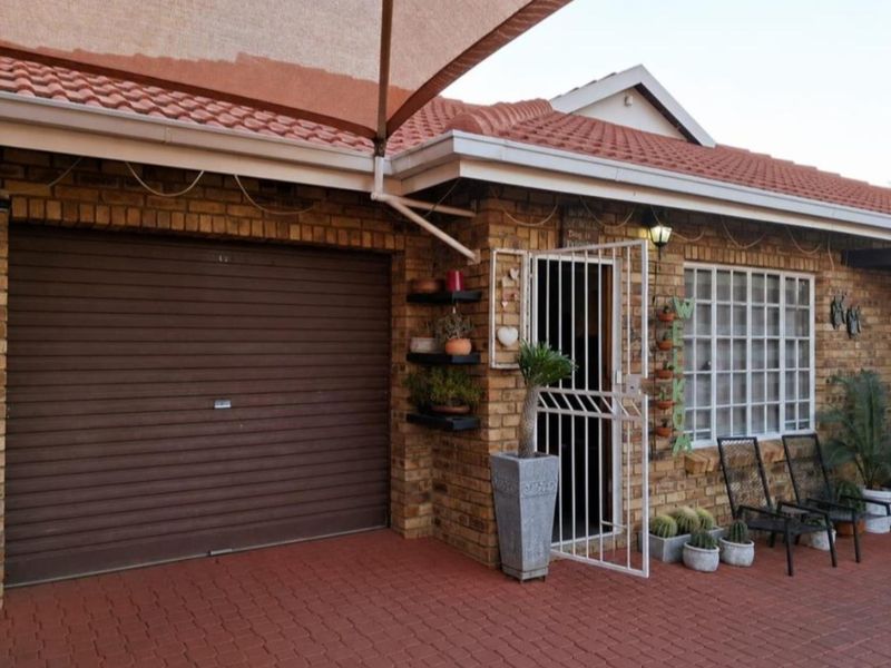 Front elevation of a face brick house featuring a roll-up garage door, paved driveway, and a covered entrance with security gate.