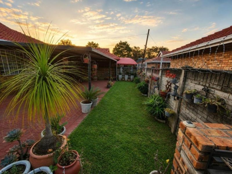 A well-maintained rear garden featuring a covered patio, brick paving, a built-in braai, and a lawn area enclosed by brick boundary walls.
