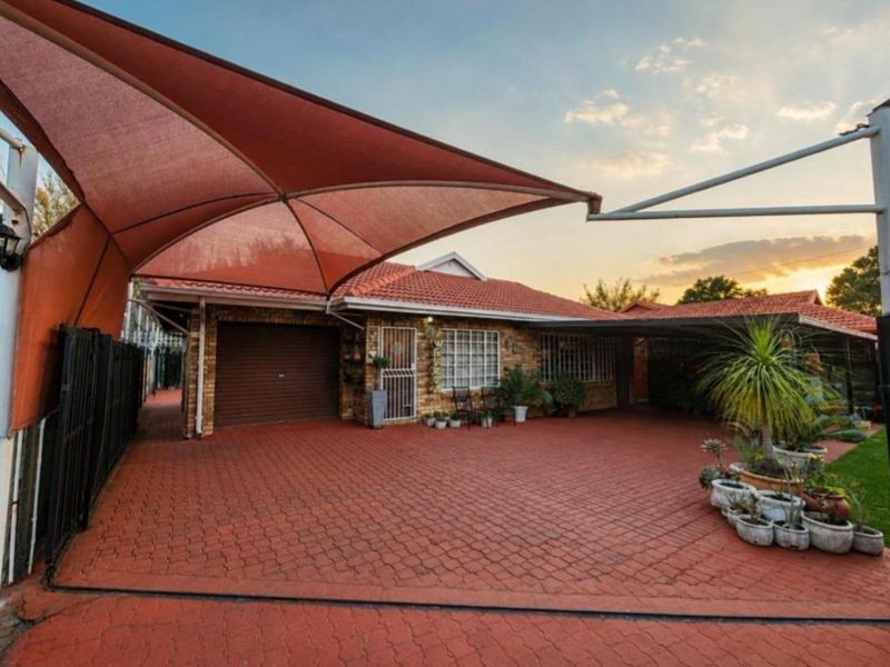 Front exterior view of a brick house featuring a paved driveway, integrated garage, and a large shade sail structure providing covered parking.