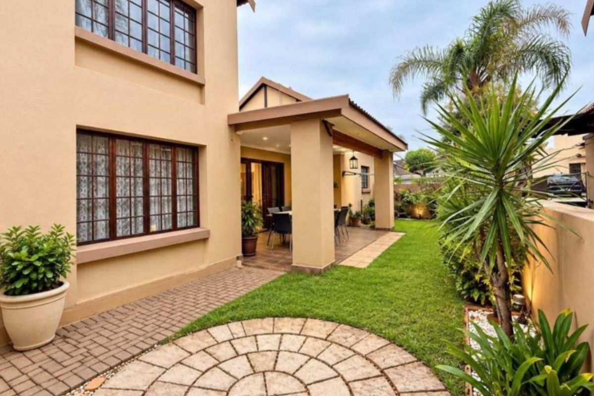 A well-maintained rear exterior featuring a covered patio, paved circular feature, and landscaped garden area with established greenery.