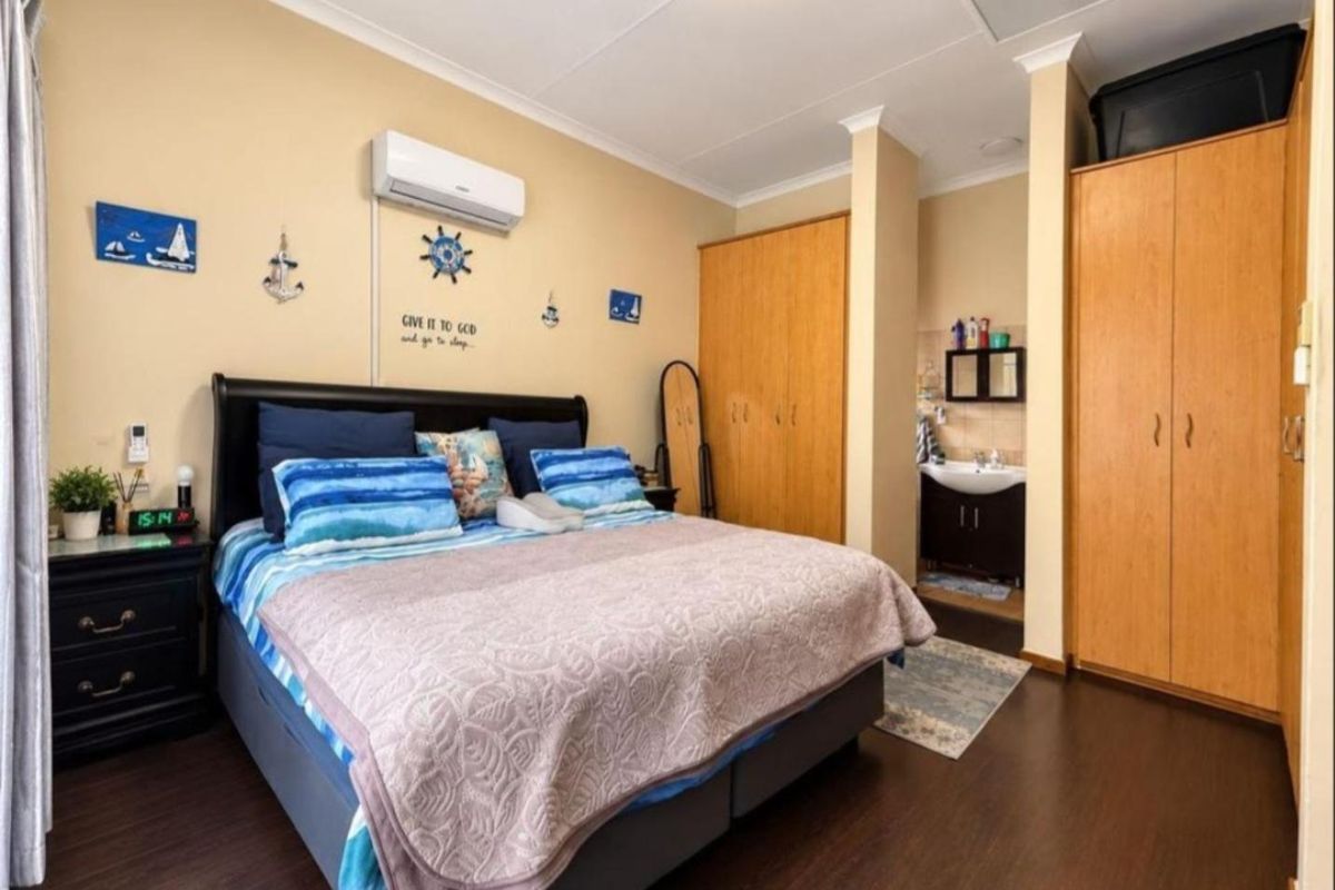 Spacious bedroom featuring laminate flooring, built-in cupboards, a wall-mounted air conditioner, and a convenient en-suite vanity area.