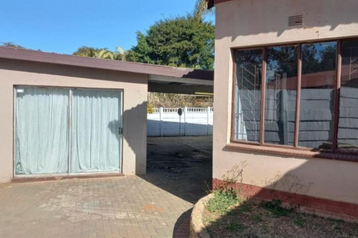 Rear exterior view showing a paved courtyard area, carport, and access to the main dwelling via a sliding glass door.