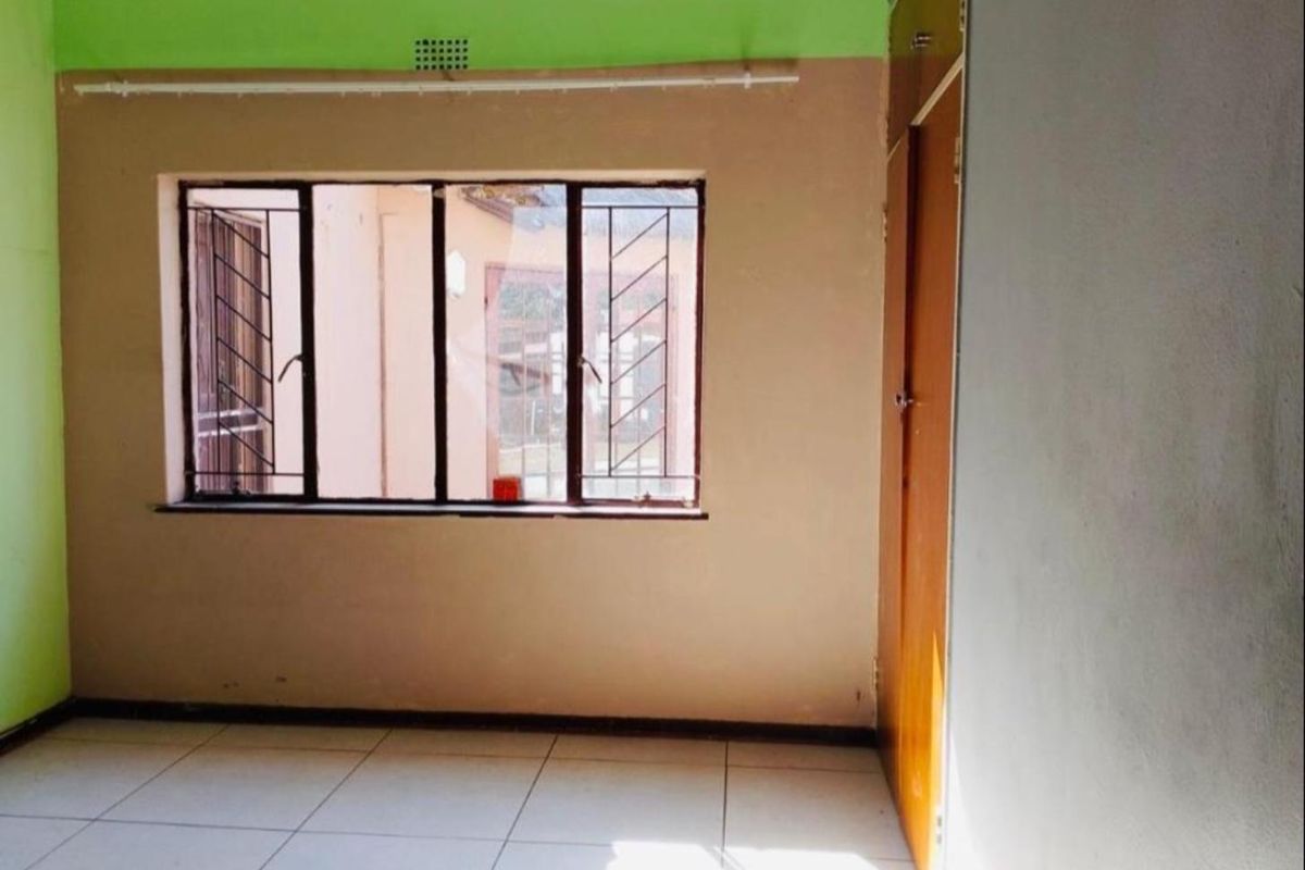An empty bedroom featuring tiled flooring, a built-in cupboard, and windows fitted with security bars.