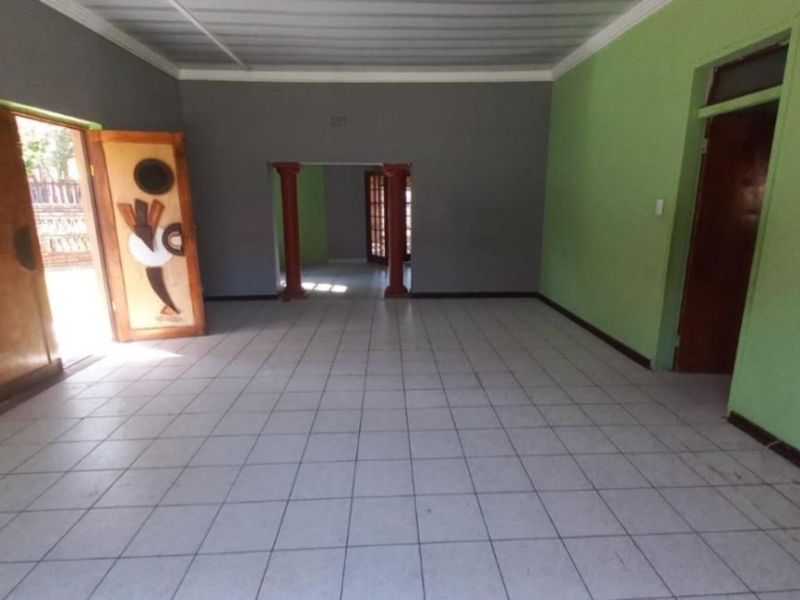 An empty, open-plan living area featuring ceramic floor tiles, decorative wooden doors, and structural columns, offering a blank canvas for renovation.